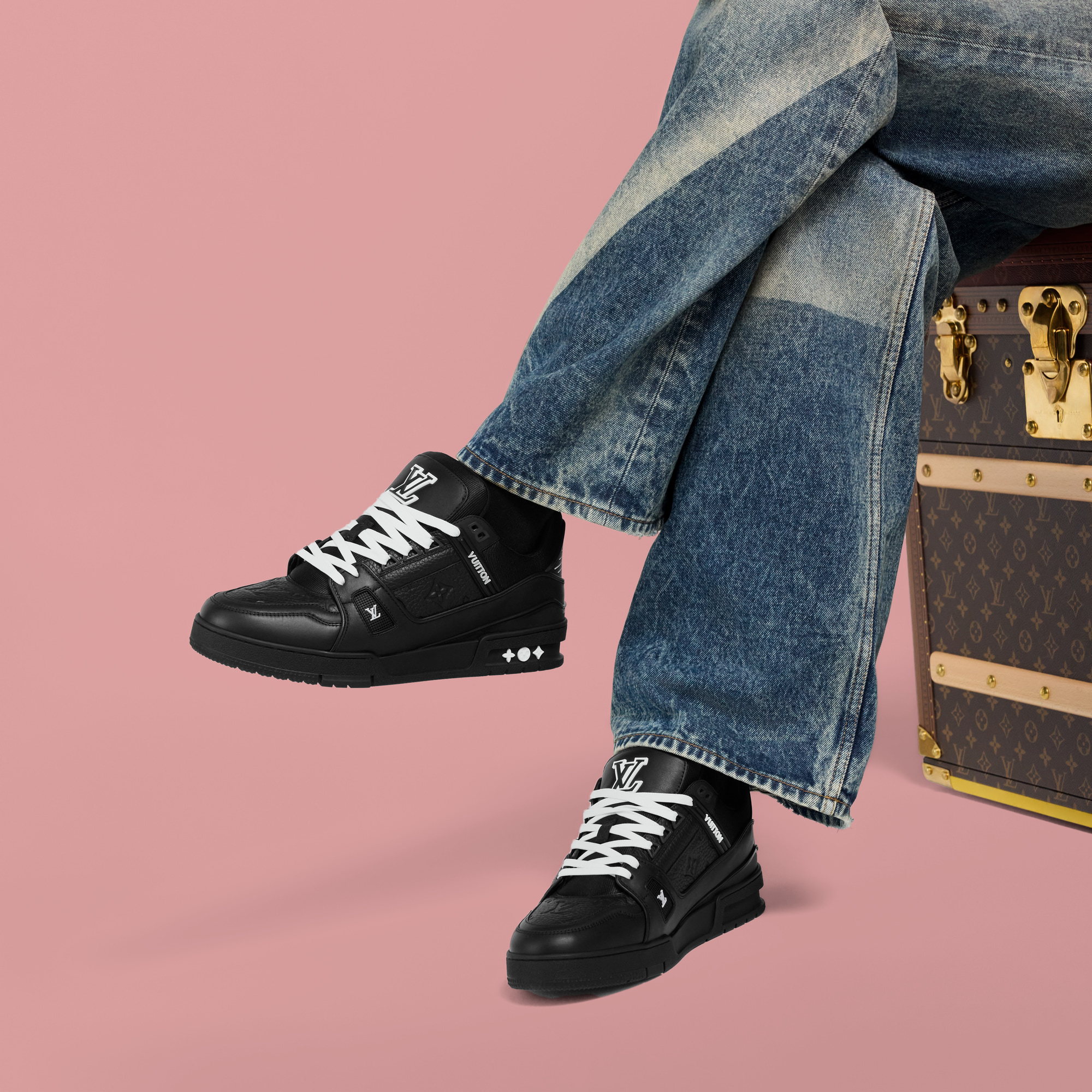 Black LV sneakers with white laces worn with blue jeans against a pink background